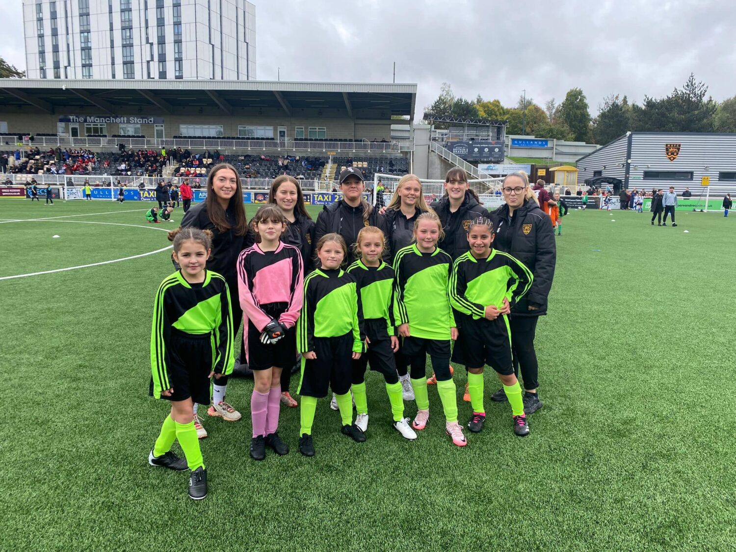 Students in football kits smiling for a photo with some of the women's team at Maidstone Stadium