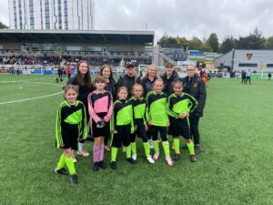 Students in football kits smiling for a photo with some of the women's team at Maidstone Stadium