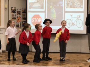 5 children laughing, one holding a stop sign, one wearing glasses, one wearing fake ears, one wearing a hat, and one wearing a giant foam hand