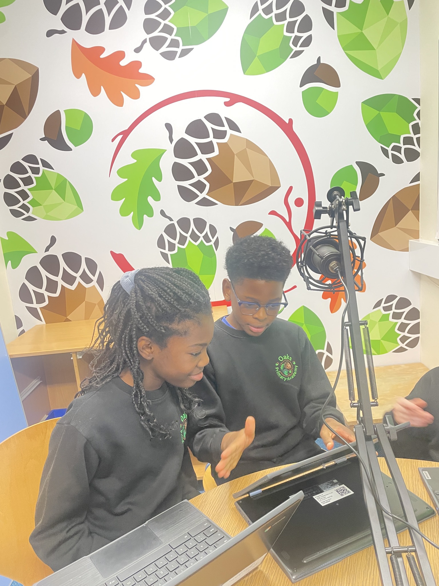 2 students looking at a laptop, behind a microphone