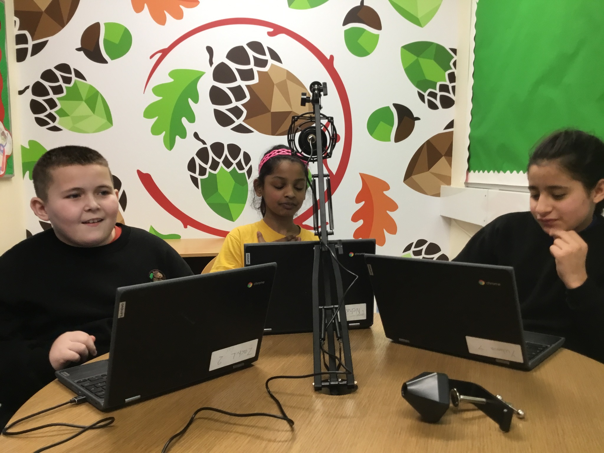 3 students looking at laptops, behind a microphone