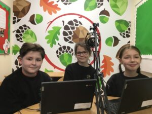 3 students smiling, sat behind a microphone