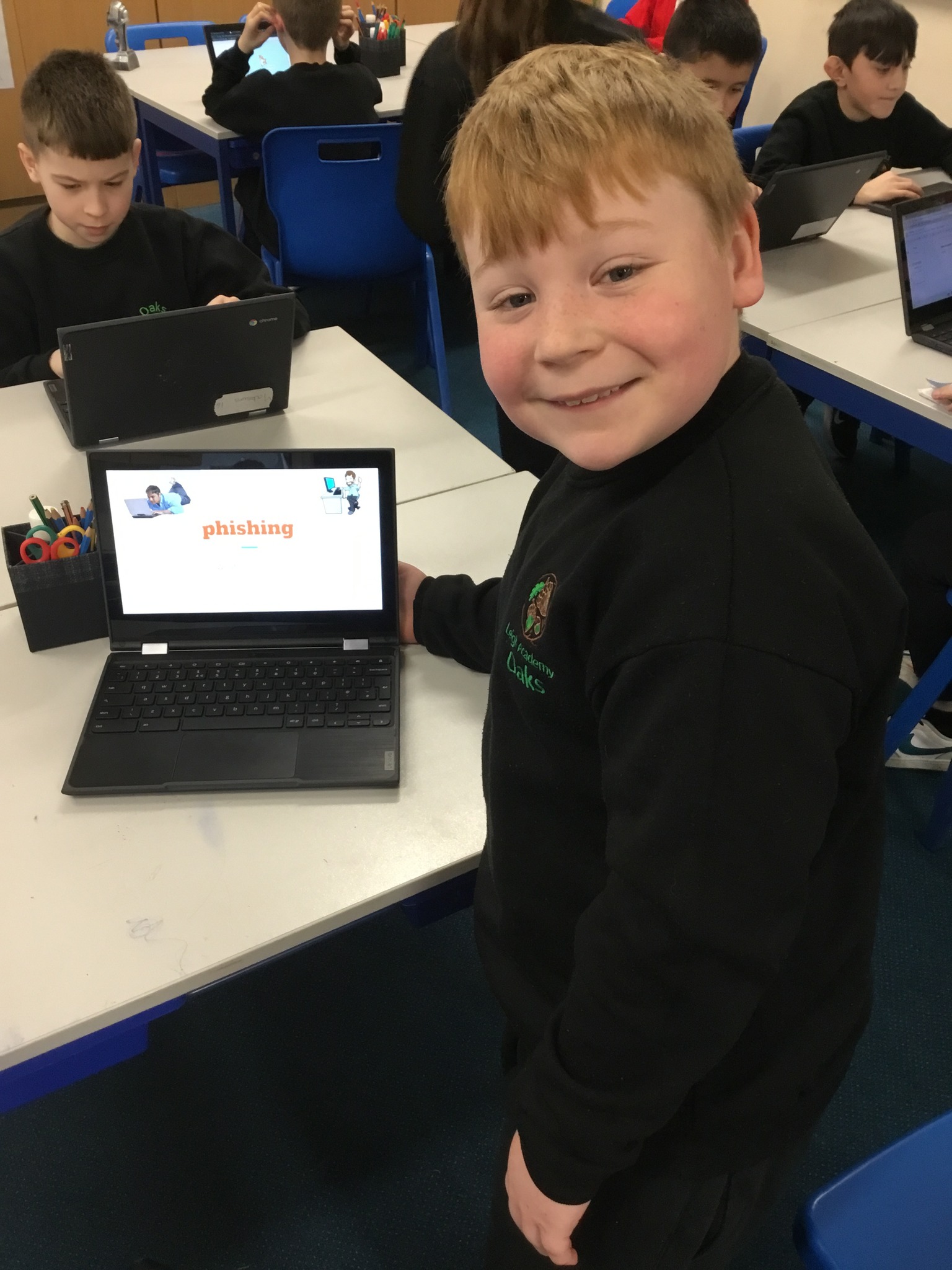 A student smiling next to a laptop, with the screen showing the word 'phishing'